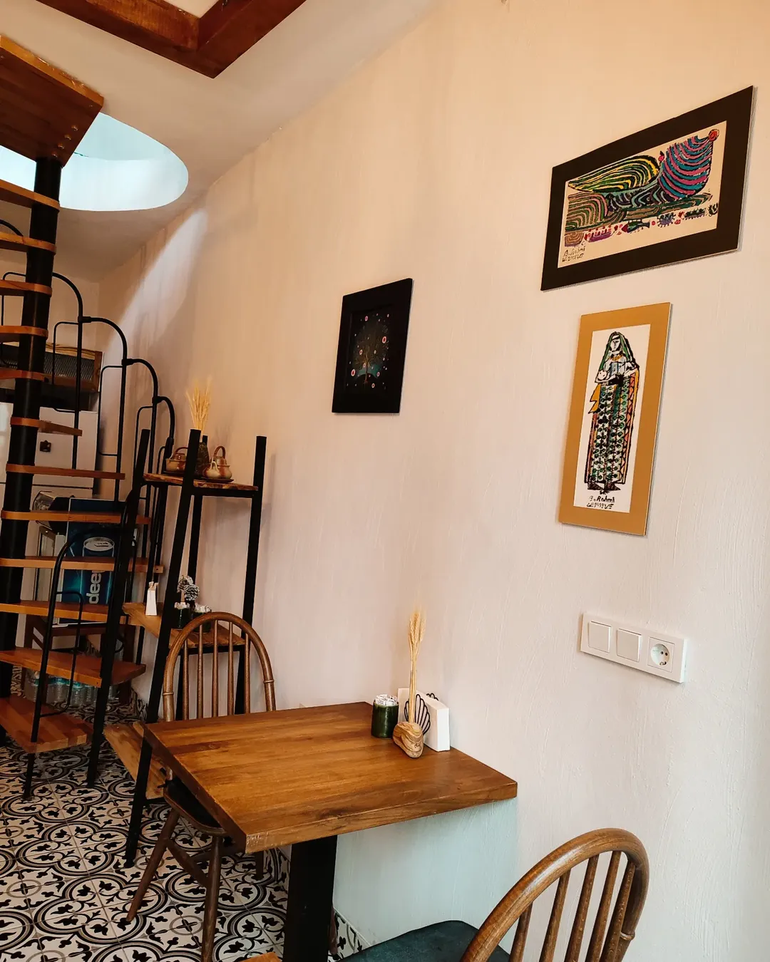 Akida Kafe’de ahşap masa düzeni, spiral merdiven ve duvar tablolarıyla öne çıkan iç mekan köşesi